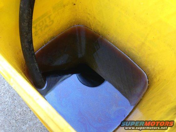 Yellow bucket with dark used oil and a black hose. Supermotors.net logo at bottom right