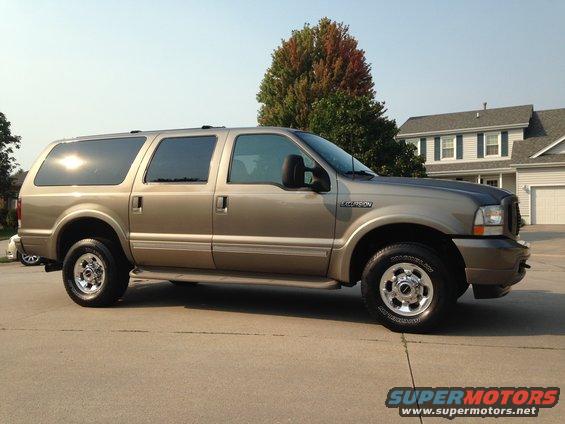 Side view of a gold 2003 Ford Excursion parked on a driveway in front of a house