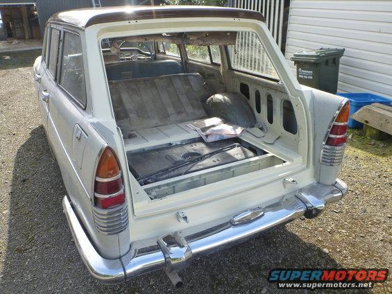 Rear view of a white station wagon with its trunk open. The interior is visible, showing folded seats and a spare tire well
