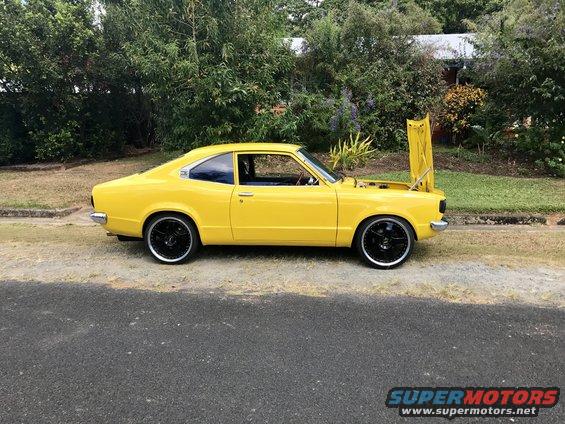 Yellow 1973 Mazda RX-3 coupe parked roadside with hood open, black rims