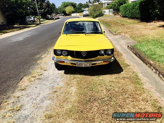 Yellow 1973 Mazda RX-3 coupe parked on a residential street, front view