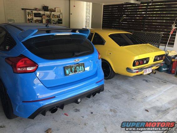 Yellow 1973 Mazda RX-3 coupe and blue Ford Focus RS parked in garage