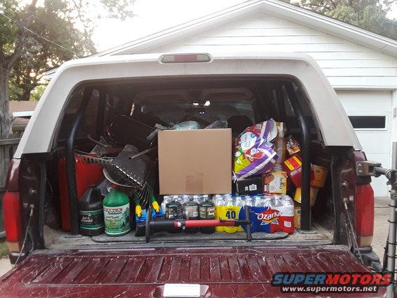 Rear view of a pickup truck bed loaded with groceries, gardening supplies, and a box
