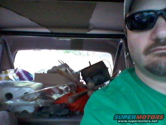 Interior view of a vehicle with a person in sunglasses, loaded with various items and equipment