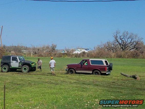 Maroon Ford Bronco and black Jeep Wrangler parked in a grassy field with two men standing nearby