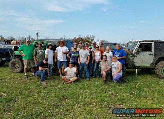 Group of people posing in front of muddy off-road vehicles, one is green and black, another is silver and black