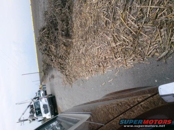 View from inside a vehicle looking out at a utility truck parked next to a pile of dried corn stalks