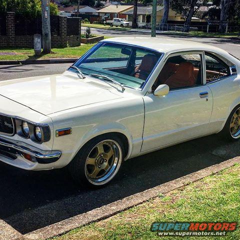 White coupe parked on street, tan interior visible. Aftermarket wheels