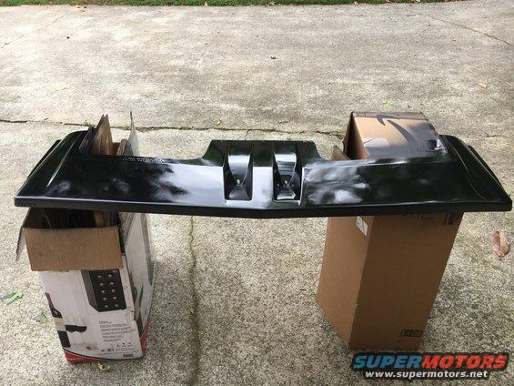 Black plastic car bumper part resting on cardboard boxes