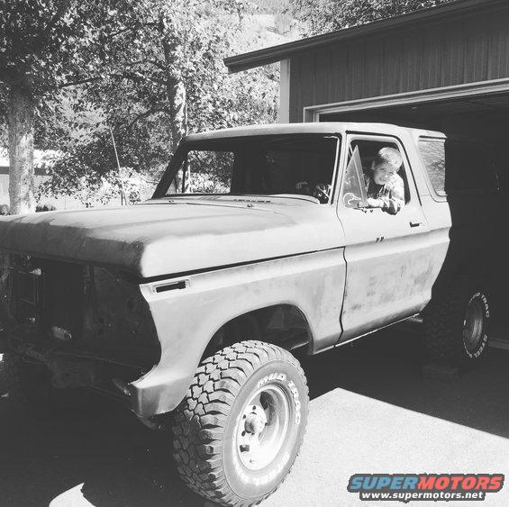 Kid in driver's seat of a 1978 Ford Bronco parked outside a garage