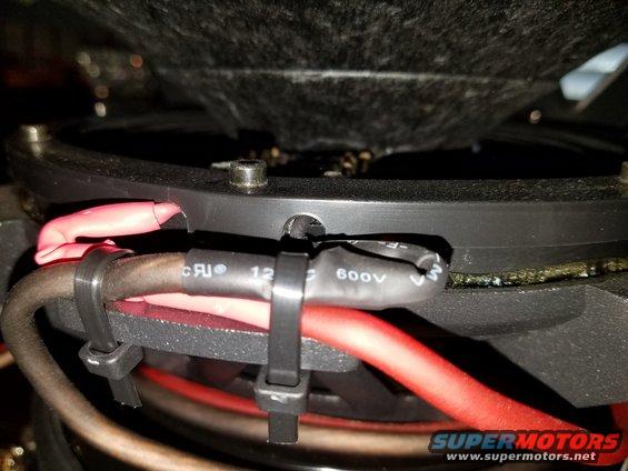 Close-up of car subwoofer wiring with red and black cables, zip-tied together. Heat shrink tubing on one cable shows "600V"