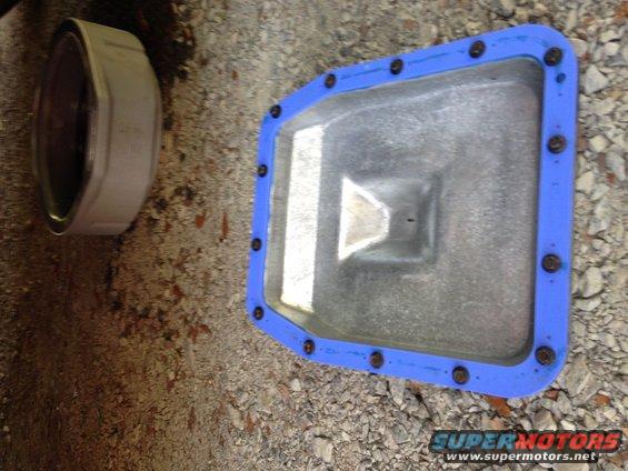 Metal oil pan with blue gasket and bolts, next to a round metal object