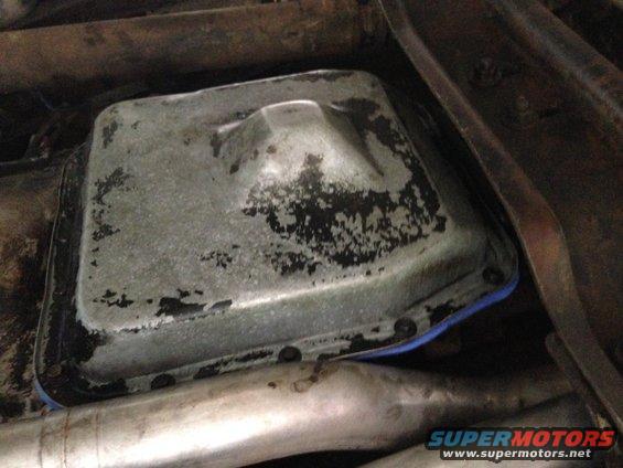 Oil pan with blue gasket and black grime, viewed from below with exhaust pipes
