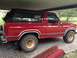 1986 Ford Bronco - This red 1986 Ford Bronco features a black removable top and is parked under a covered area.