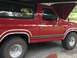 1986 Ford Bronco - The side profile of a red 1986 Ford Bronco shows its distinctive body style and trim.