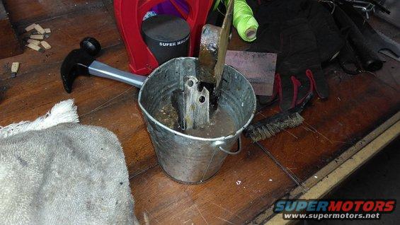 Metal part soaking in a bucket with a hammer and brush nearby
