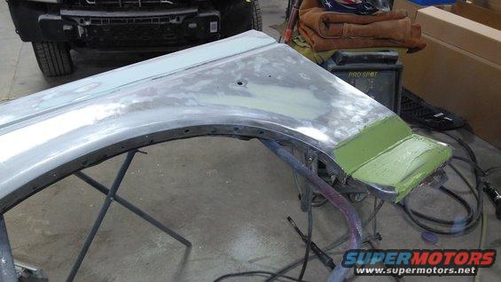 Car fender on stand with body filler applied, front of another vehicle in background