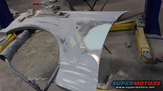 Car fender with body filler and sanding tools, held by a stand in a workshop
