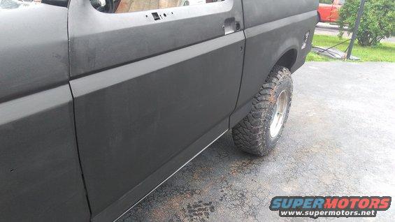 1996 Ford Bronco side panel with primer, showing front door seam and rear fender. Off-road tire visible