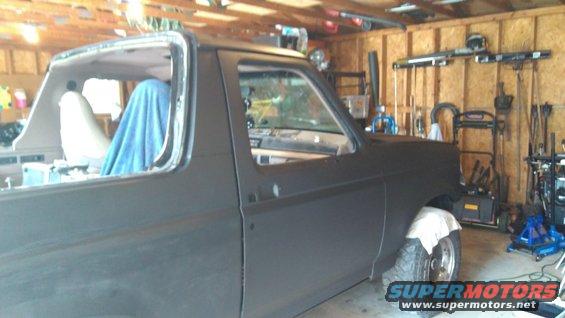 Side view of a dark-colored Ford Bronco with its top removed, parked in a garage with tools and equipment visible