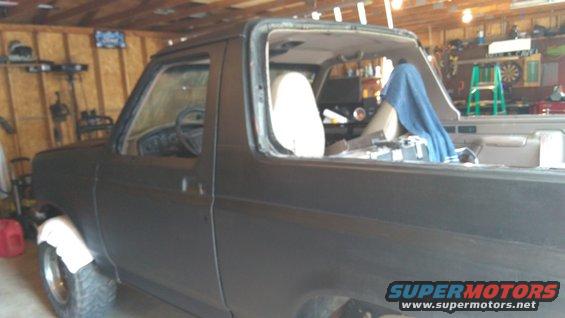 Dark gray Ford Bronco in a garage, undergoing repairs, with the windshield removed
