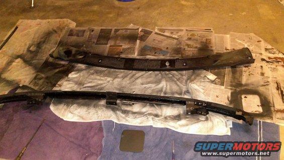 Two black car parts, possibly bumpers or trim, laid out on newspaper and drop cloths, with spray paint residue