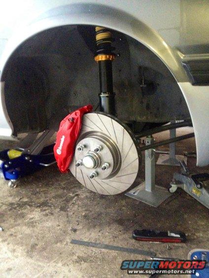 Close-up of a silver car's front brake rotor with a red caliper, supported by jack stands