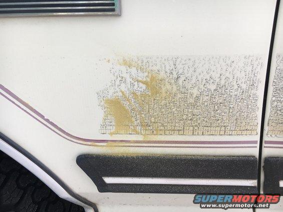 Faded decal with sand residue on white vehicle side panel, showing purple stripe detail