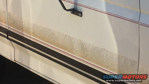White 1988 Ford Bronco side door with red and black trim, covered in mud splatter