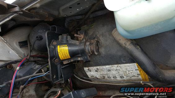 Engine bay with black jack mechanism, yellow caution label, and blue fluid reservoir