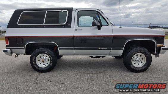 Side view of a two-tone SUV with a black camper shell. It has a black stripe with a red pinstripe separating the silver and black paint