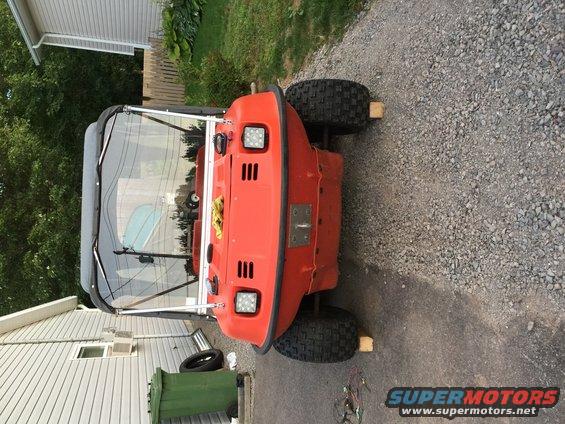 Orange amphibious ATV with a black canopy, parked on gravel. It has four large tires and square headlights