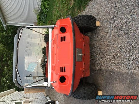 Orange amphibious vehicle with black top and windshield, parked on gravel