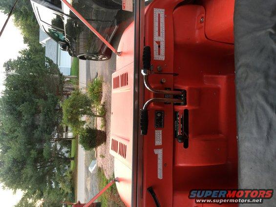 Red vehicle interior with two levers and a black fabric cover. A black SUV is visible outside
