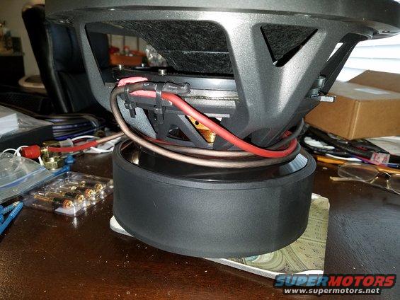 Car subwoofer with red and brown wires connected. Batteries and other car audio parts are on the table