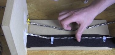 Audio speaker wire being secured with zip ties to a black foam pad on a wooden board