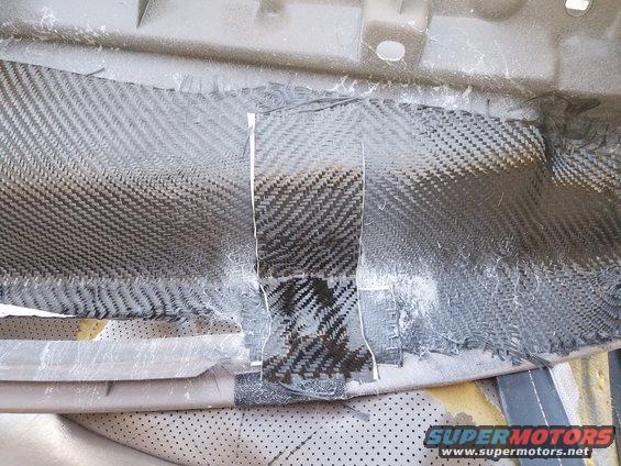 Dashboard interior with carbon fiber patch repair, showing woven texture and torn edges