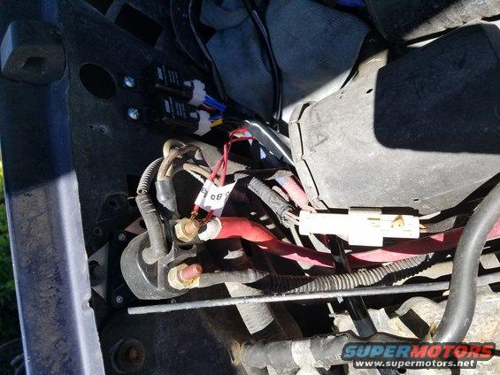 Close-up of engine bay wiring with red and black cables, two black relays, and a white connector
