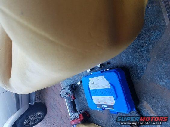 Impact wrench and blue tool case on floor next to a car seat and tire