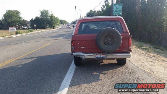 Red Ford Bronco parked on the side of a road, spare tire mounted on the rear door