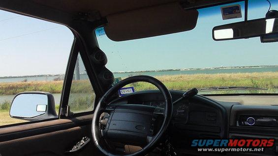 1996 Ford Bronco interior showing steering wheel, dashboard, and side mirror with a view of water outside