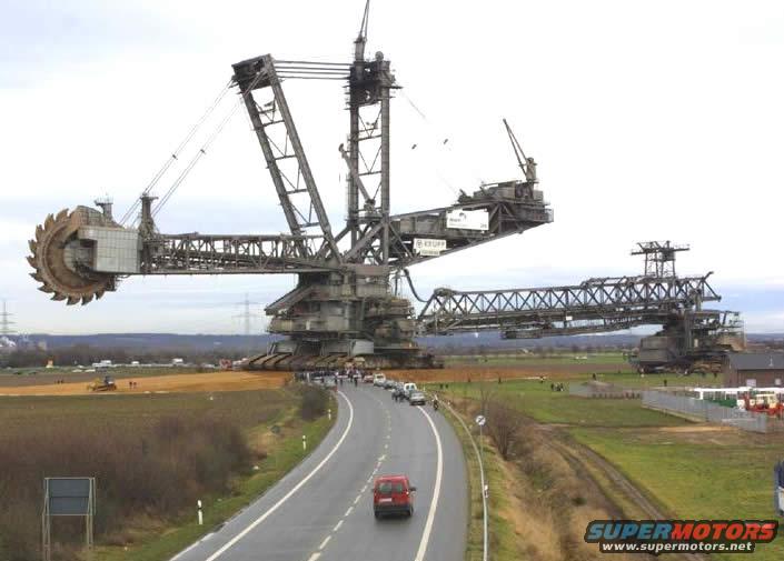 Giant bucket-wheel excavator with a road and a red car in the foreground