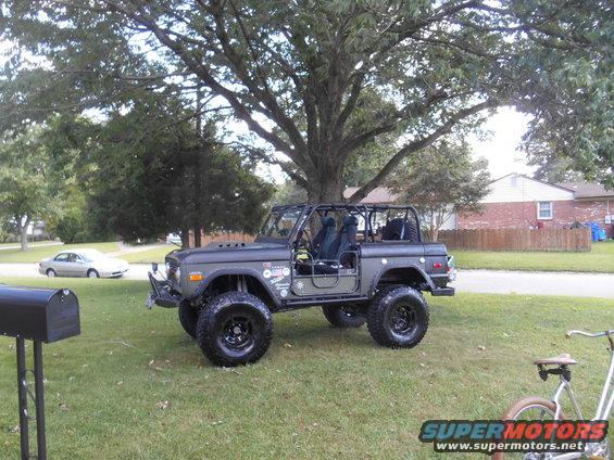 Dark gray 1972 Ford Bronco with roll cage and lifted suspension parked on grass