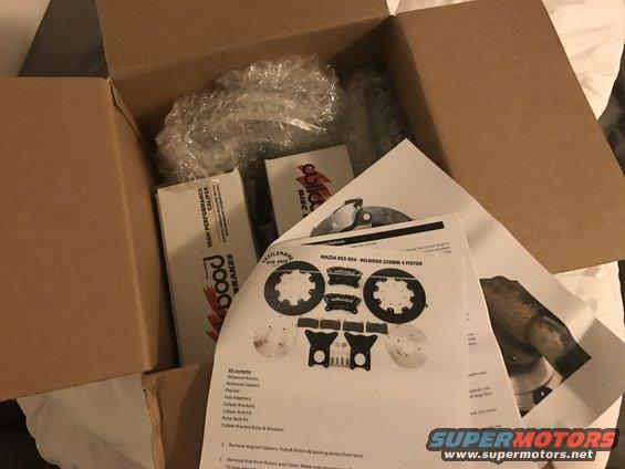Box of car brake parts, including rotors, calipers, and instructions labeled for Mazda RX3-RX4