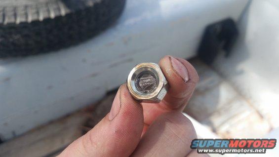 Hand holding a lug nut with a tire and white vehicle bed in background