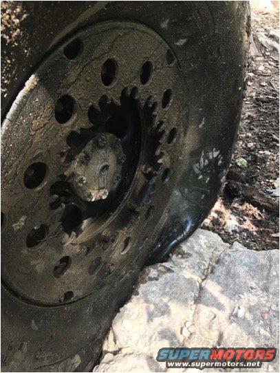 Close-up of a muddy off-road tire with a visible gear mechanism, resting on rocks