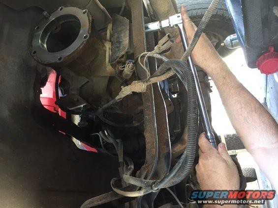 Undercarriage of a vehicle with a transmission adapter plate being bolted on. Rusty metal parts and wiring are visible