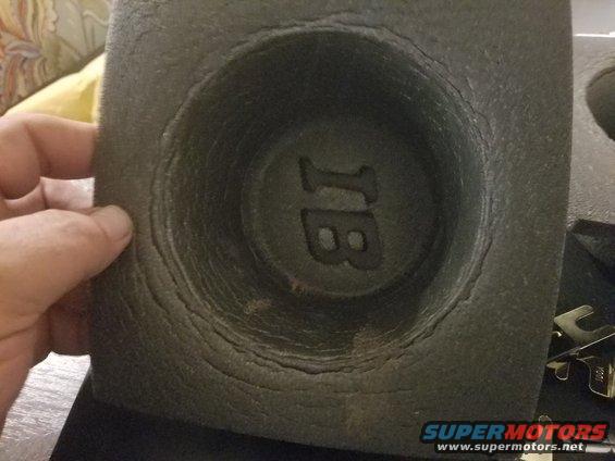 Speaker housing with cracked texture and embossed 'JB' logo, held by a hand