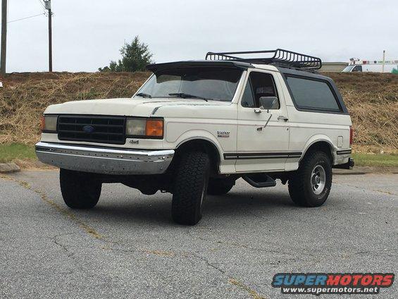 White Ford Bronco with a roof rack and a sun visor, seen from a 3/4 front angle