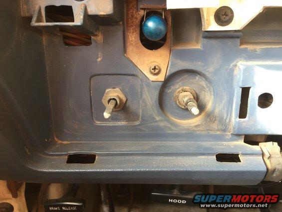 Dashboard interior showing two knobs, a blue ball-shaped object, and a switch. Text reads 'HOOD' and 'BRAKE RELEASE'